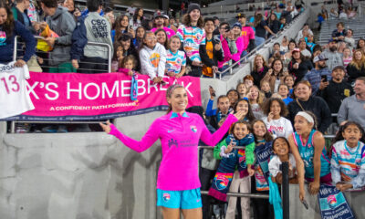 Alex Morgan standing in front of a group of fans in the stands and a sign that says Homebreak.