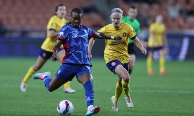 A player in a blue jersey tries to keep the ball as a player in a yellow jersey approaches her on a soccer field